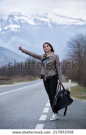 Young woman hitchhiking on countryside road.Traveler woman hitchhiking along lonely road.Pretty young woman tourist hitchhiking.Left alone on the road and lost