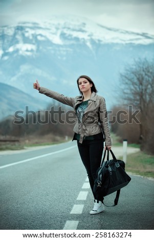 Young woman hitchhiking on countryside road.Traveler woman hitchhiking along lonely road.Pretty young woman tourist hitchhiking.Left alone on the road and lost