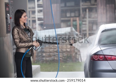 Attractive woman washing automobile at manual car washing self service,cleaning with foam,pressured water.Transportation care concept.Washing car in self service station with high pressure blaster