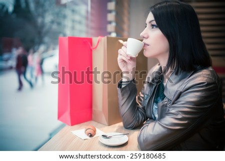 Woman with shopping bags in mall cafe drinking coffee.Shopaholic woman.Woman sitting alone in cafe.Businesswoman relaxing and enjoying after work,having a beverage.Image toned, noise added