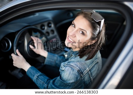 Happy woman in new car, indoor keeps wheel, turning around,smiling.Young woman in car going on road trip.Learner driver student driving car.Driver license exam