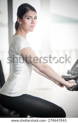 Woman riding an exercise bike in gym.Doing sport biking in the gym for fitness.Cardio and fat loss workout in the gym.Athletic woman pedaling on a stationary bike.Sport and fitness,summer body goals