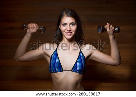 fitness, sport, power lifting and people concept-sporty woman exercising.Low key fitness woman working out with dumbbells.Young adult fitness woman doing exercises fitness workout.Power and strength