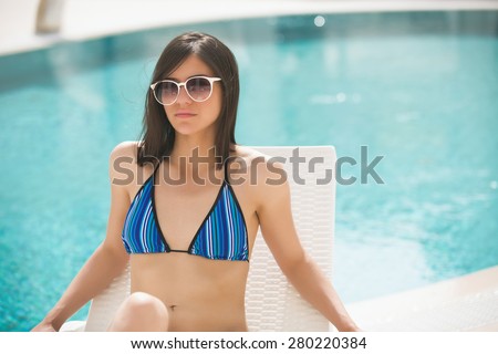 Sexy beautiful brunette woman with in bikini relaxing beside a swimming pool in summer on tropic island in hot weather on pool party.Woman relaxing in deck chair.Sunscreen,protection,summer