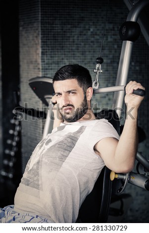 Man using pull down machine in gymnasium.Handsome muscular man exercising on pull down machine. Young man on pull down machine in full force.Young man working back muscles on seated pull down machine