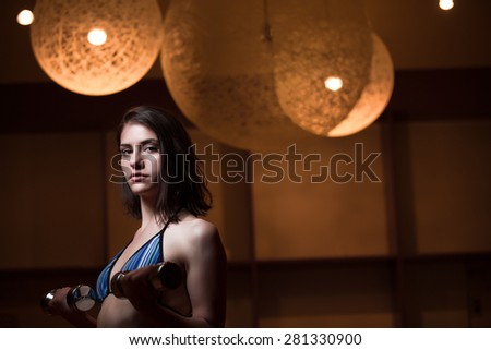 Fitness, sport, power lifting and people concept-sporty woman exercising.Low key fitness woman working out with dumbbells.Young adult fitness woman doing exercises fitness workout.Power and strength