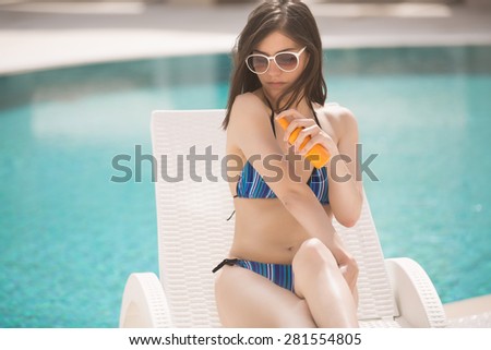 Woman applying sun cream to prevent sun spots,melanoma and UV radiation.Sexy brunette woman with in bikini relaxing beside a swimming pool in summer on tropic island.Sunscreen,protection,summer body