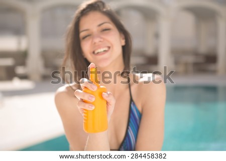 Smiling woman with sun creme.Young beautiful cheerful tanned woman with sun UV  high SPF protection cream.Sunscreen.Sunblock.Woman showing solar cream by the pool on sunny summer day.Focus on cream