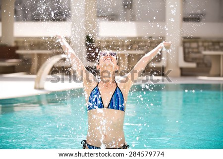 Young beautiful woman making water splash in sexy bikini at the pool.Enjoying summer.Young slim fit tanning woman having fun in poll and making water splash with hands