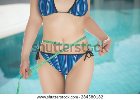 Attractive girl in bikini with tape-measure at the sea side.Slim fit woman at the beach in bikini with measure tape.woman measure waist, perfect slim body figure, female measuring tape size of belly.