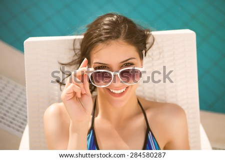 Sexy beautiful brunette woman with sunglasses in bikini relaxing near swimming pool in summer on tropic island in hot weather .Woman relaxing in deck chair.Sunscreen,protection,summer body