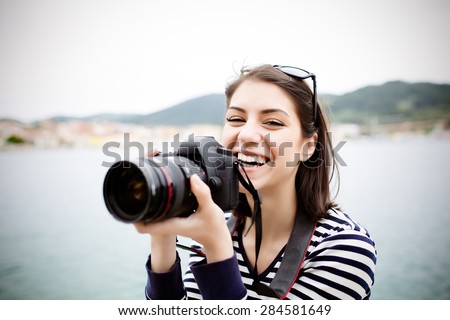 Happy woman on vacation photographing with a dslr camera on the beach and smiling