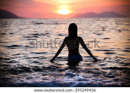 Gorgeous sexy fit woman silhouette swimming in sunset.Free happy woman enjoying sunset. Beautiful woman in water embracing the golden sunshine glow of sunset, enjoying peace, serenity in nature.