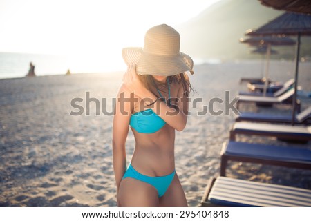 Sexy tanned female on the beach,beautiful slim woman on seashore,enjoying  summer day,wearing hat and swimsuit, near beach deckchairs and sunshades,beach party, summer vacation concept