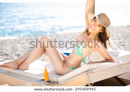 Smiling beautiful fit woman sunbathing in a bikini on a beach at tropical travel resort,enjoying summer holidays.Young woman lying on sun lounger near the sea.Happy cheerful girl having SPF protection