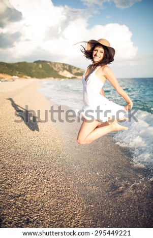Woman jumping in the air on tropical beach,having fun and celebrating summer,beautiful playful woman in white dress jumping of happiness.Active lifestyle, summer holidays and vacation concept.Freedom