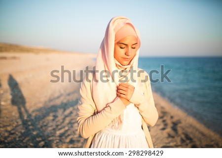 Muslim woman on the beach spiritual portrait.Humble muslim woman praying on the beach.Summer holiday,muslim woman walking on the beach