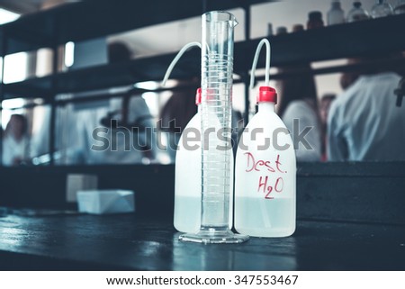 Distilled purified deionised water in plastic bottles with a pump. Measuring graduated cylinder for measuring water volume. water fro scientific research and experiments. Water for chemical solutions