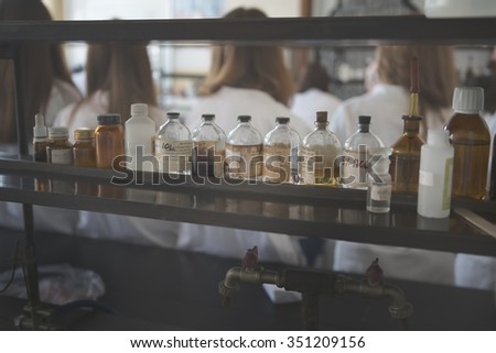 Chemicals and laboratory utensils.Vintage pharmacy bottles on wooden board.Chemical bottles for use on chemistry class.Safe chemicals for organic chemistry lab.Students blurred in the background