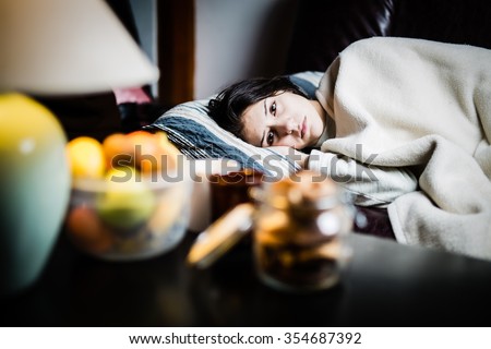 Sick woman in bed,calling in sick,day off from work.Thermometer to check temperature for fever.Vitamins and hot tea in front.Flu.Woman Caught Cold.Virus.Sick woman laying in bed under wool blanket