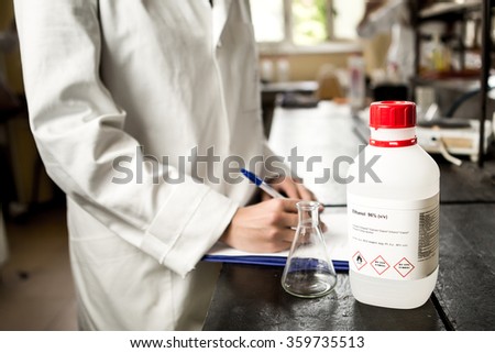 Scientist conducting research taking notes while looking progress.Science, chemistry,medicine and pharmacy concept-young scientist writing observation.Chemicals and laboratory utensils.Chemical bottle