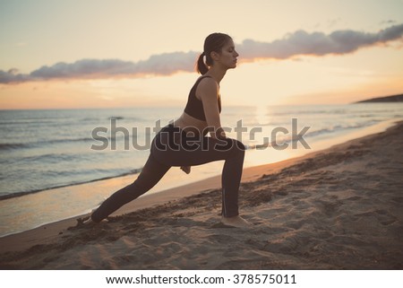 Runner woman doing stretching exercises at sunset on the beach.Young fit healthy woman practicing yoga and pilates.Healthy lifestyle and regular exercising routine.Body and soul harmony and relaxation