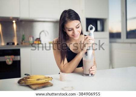 Woman with hand blender making sweet banana chocolate protein powder milkshake smoothie.Drinking protein shake after workout.Whey,banana,low fat milk sport nutrition diet after gym.Healthy lifestyle