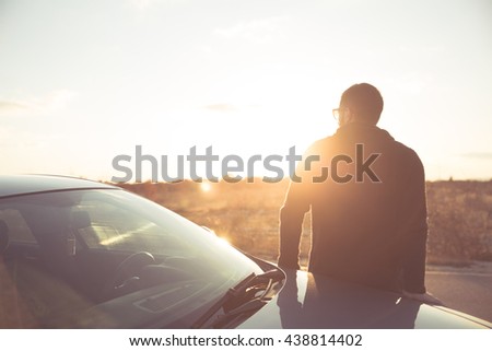 Road trip break after long drive.Young stylish man enjoys sunset.Young man fascinated by illuminated nature, escape from everyday job problems. Open field delight of natural beauty view.