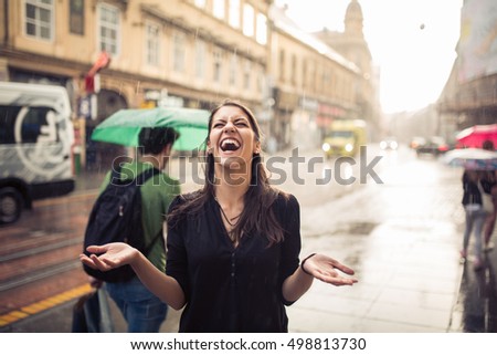 Woman stands under the rain screaming and enjoying.Portrait of young beautiful  wet woman standing on the street with her hands spread enjoying rain falling on her.Refreshment enjoying life concept