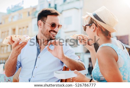 Beautiful loving couple sitting on the bench in the center of the city and eating pizza. Lifestyle concept