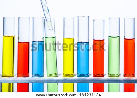 Laboratory pipette with drop of liquid over set of test lab tubes with color liquid on stand