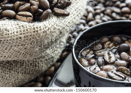 Cup of coffee beans with spilled coffee beans and bag full of coffee beans