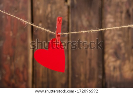 One red heart hanging on the clothesline. On old wood background. Valentine\'s day decoration.