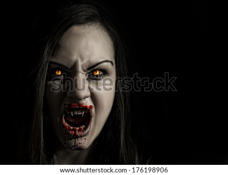 Bloodthirsty female vampire with angry expression and bloody mouth isolated on black background