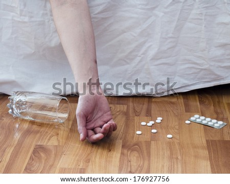 Suicide with pills. Drug abuse concept, passive hand on floor with spilled pills and glass of water