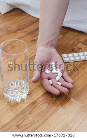 Suicide with pills. Drug abuse concept, passive hand on floor with spilled pills and glass of water