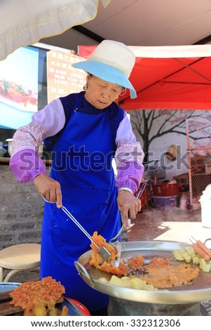 Dali (Yunnan), CHINA - October 17, 2015: A chinese nationality old women selling fried seafood. Located in Dali Ancient City, Yunnan Province, China.