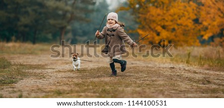 Child girl runs, has fun and plays with his dog during walk in autumn forest.