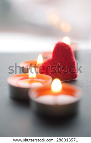 Small red felt heart are seen among burning candles prepared for romantic Valentine\'s Day