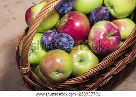 fresh plums and apples in a wicker basket