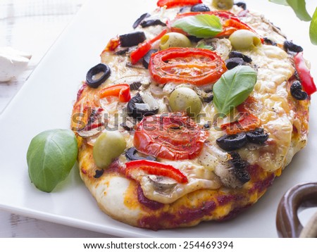 pizza with tomatoes, mushrooms, olives and peppers served on a plate on a wooden table