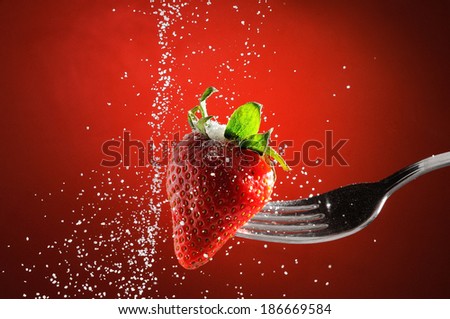 Strawberry on a fork punctured falling sugar with red background detail