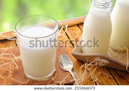 Glass of milk on a table on the field with two bottles of milk