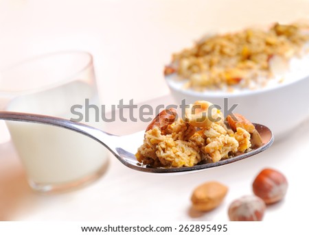 Spoon with muesli and nuts and glass of milk and cereal bowl at the bottom