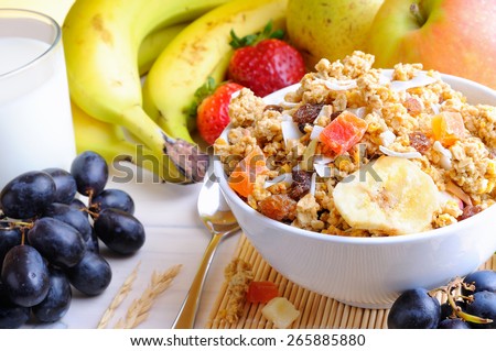 Bowl of cereal with fruit on a white wooden table and fresh fruits behind