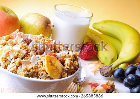 Bowl of cereal with fruit on a white wooden table and fresh fruits behind top diagonal composition