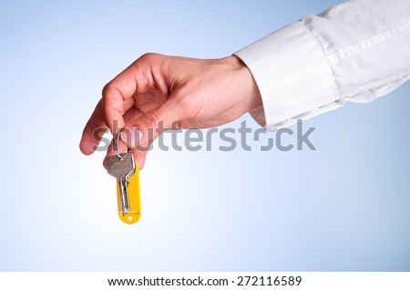 Arm of a commercial agent construction in white shirt taking some keys to provide the buyer of a house with blue gradient background