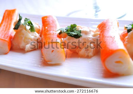 Surimi sticks with sauce on a white plate on a white wooden table front view