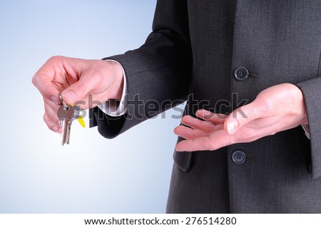 half lateral body commercial agent wearing a dark gray costume handing the keys for the purchase of a house with blue background isolated