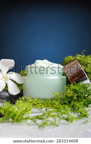 Open cream jar algae. Flowers, black stones and seaweed decoration. Blue background. Front and vertical view